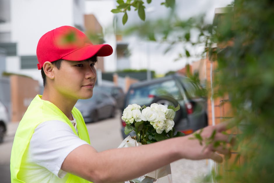 A young delivery person wearing a red cap and a neon yellow vest is seen handing over a bouquet of fresh white flowers, including roses and peonies, wrapped in light-colored paper with a white ribbon,